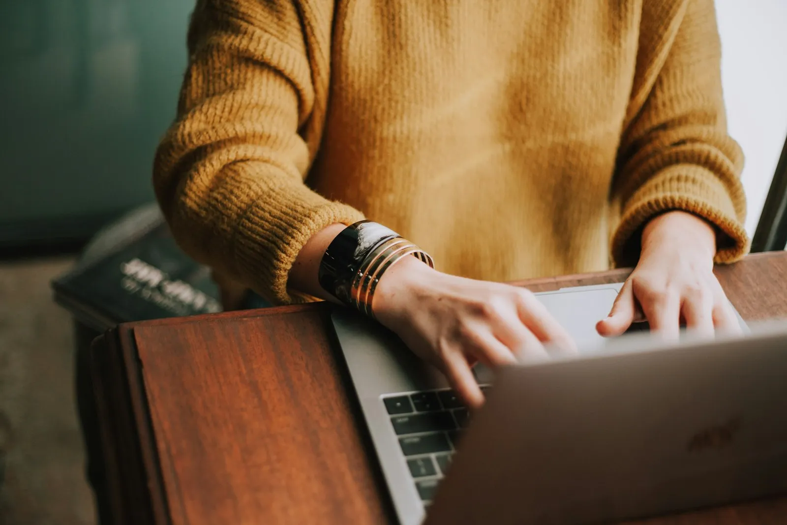 Personne en pull de laine, mains posées sur un ordinateur portable ouvert sur un bureau en bois